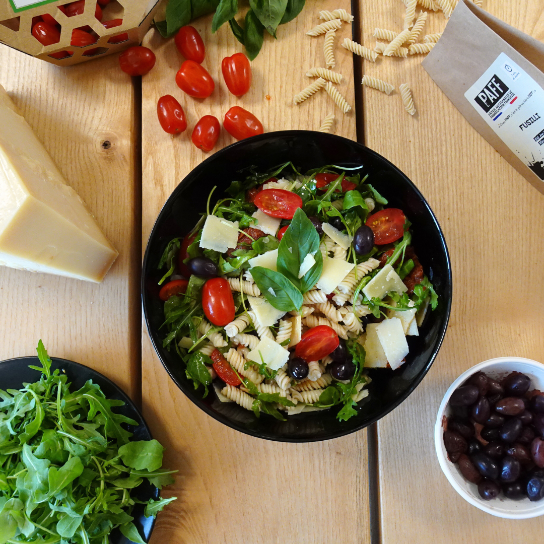 Photo d'une salade de pâtes fusilli avec tomates, tomates séchées, parmesan, roquette et olives noires